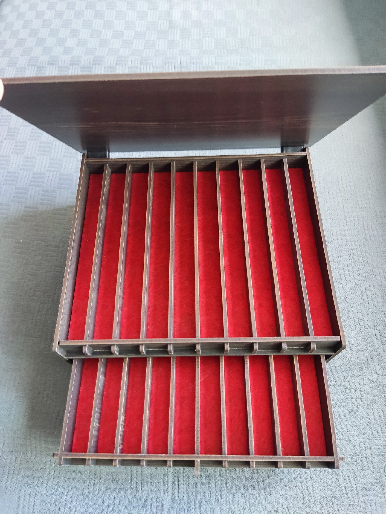 La caja anterior abierta, en la que se ven 2 bandejas con 10 huecos cada una y con el fondo de fieltro rojo