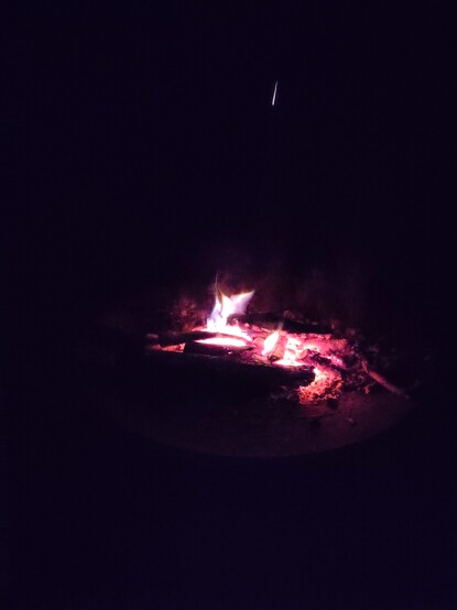 A low wood fire burns red in the darkness. A spark shoots out above and looks like a falling star.