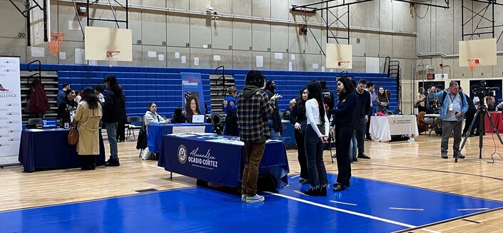 High school gym with many tables set up with kids and adults on various stem topics. Center table says Congresswoman Alexandria Ocasio Cortez 