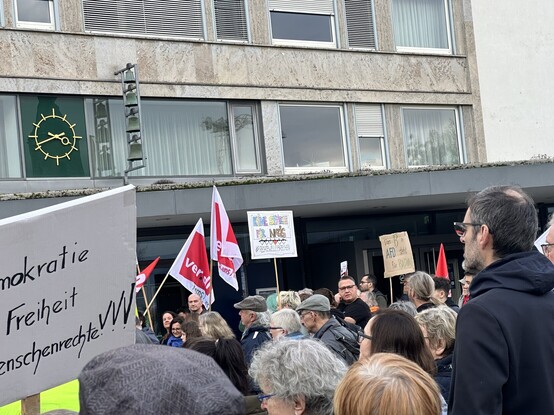 A crowd of people at a demonstration with protest signs (one saying „Keine Spätzle für Nazis“) and flags in front of a building with a distinctive clock (Rathaus Waiblingen)