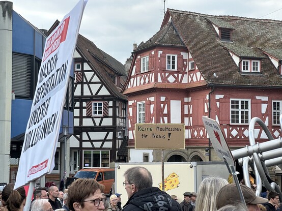 A protest crowd with banners (one saying „Keine Maultaschen für Nazis!“) in front of traditional half-timbered houses in the old town of Waiblingen.