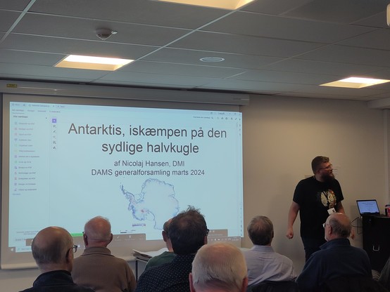 Man standing in front of slide with picture of Antarctica on it and title in Danish "Antarctica the ice giant in the southern hemisphere"