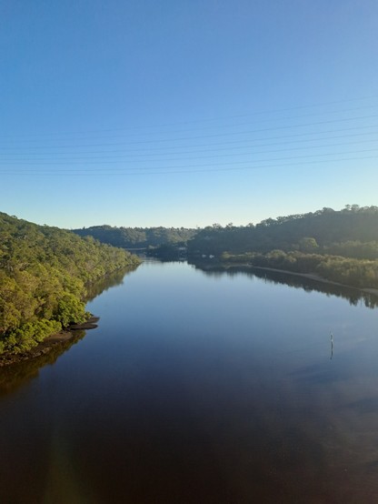 A view of a river from above, the sky is bright blue, reflected in the mirror calm river.