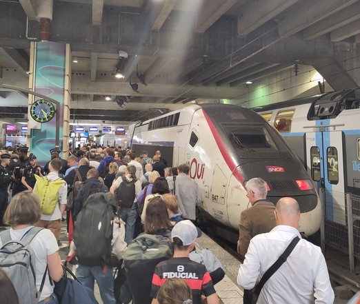 A crowd at a train station, a white and red high-speed train.