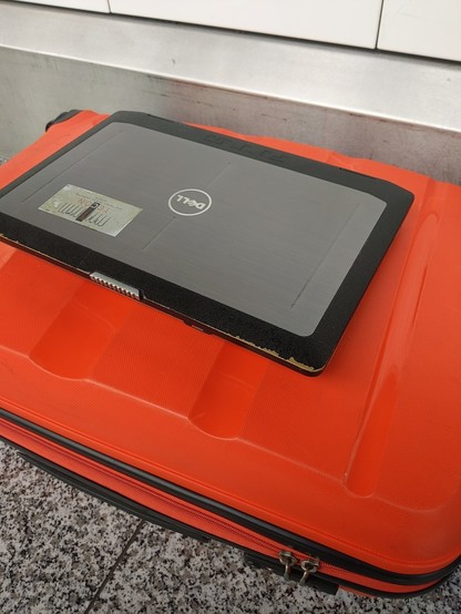 Dell Latitude E6430 ATG semi-rugged laptop on top of a bright orange hard-shell suitcase.