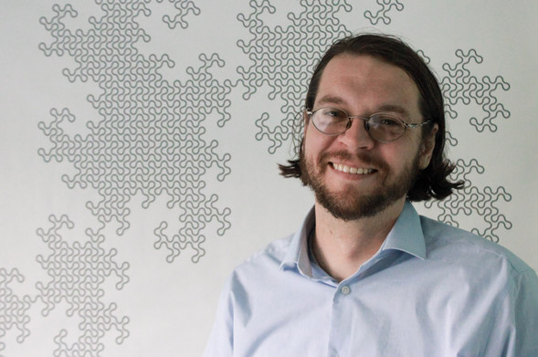 A head shot of Chris Orban standing in front of a 13th order dragon fractal
