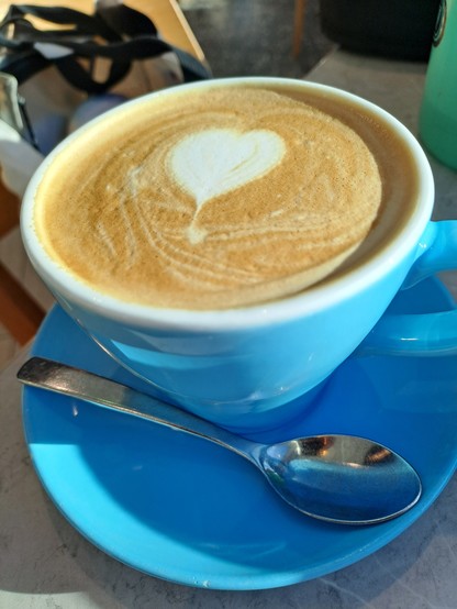 A flat white with a heart in the foam, in a blue mug on a blue saucer.