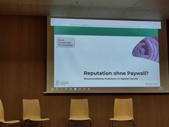 Leere Stühle vor Folie der Tagung „Reputation ohne Paywall. Wissenschaftliches Publizieren im digitalen Wandel“ an der ULB Darmstadt